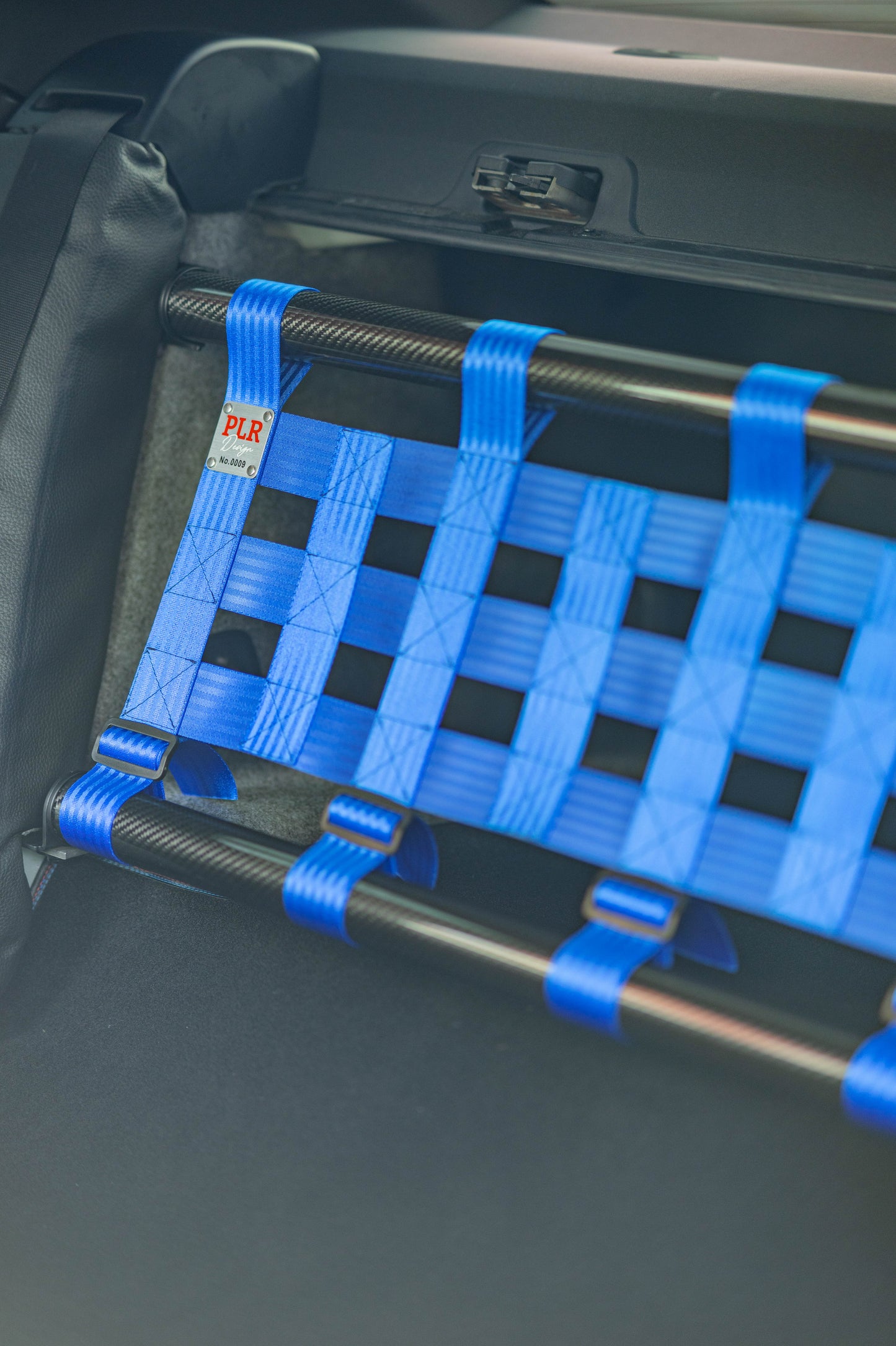 Clubsport-Set für BMW 3 E92 mit Carbon-Strebe und Netz, montiert anstelle der Rücksitzbank für Gewichtsreduzierung und klare Innenraum-Trennung. Ansicht: Detail von PLR Design Plakette.